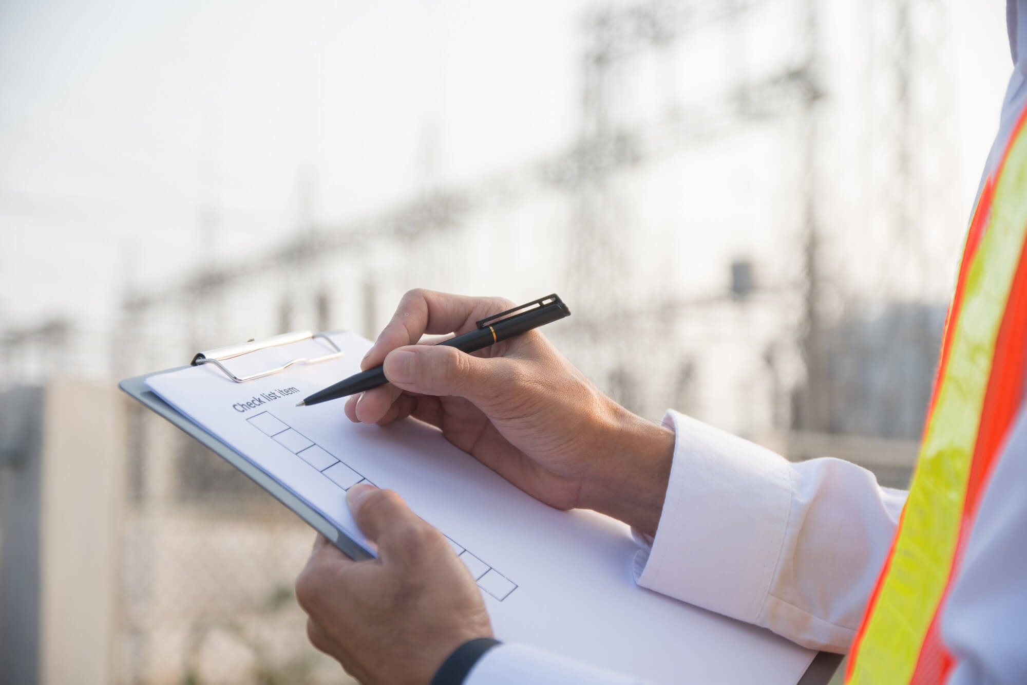 Henkilö täyttää tarkastuslistaa kynällä ulkona rakennustyömaalla.