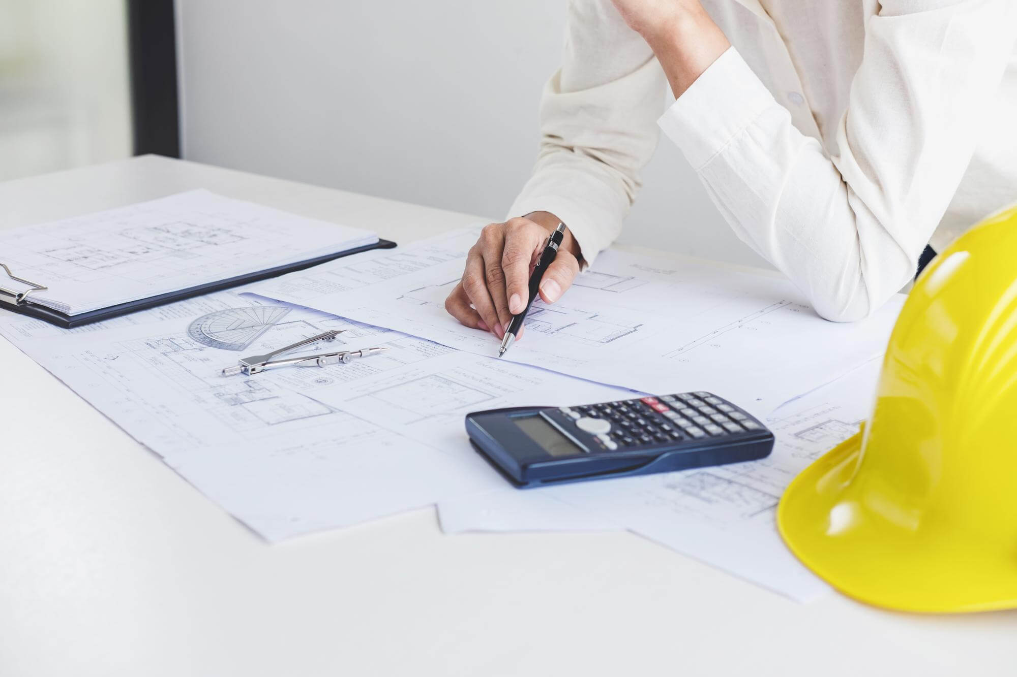 Insinööri tarkastelee piirustuksia, joiden päällä on laskin ja keltainen suojakypärä.